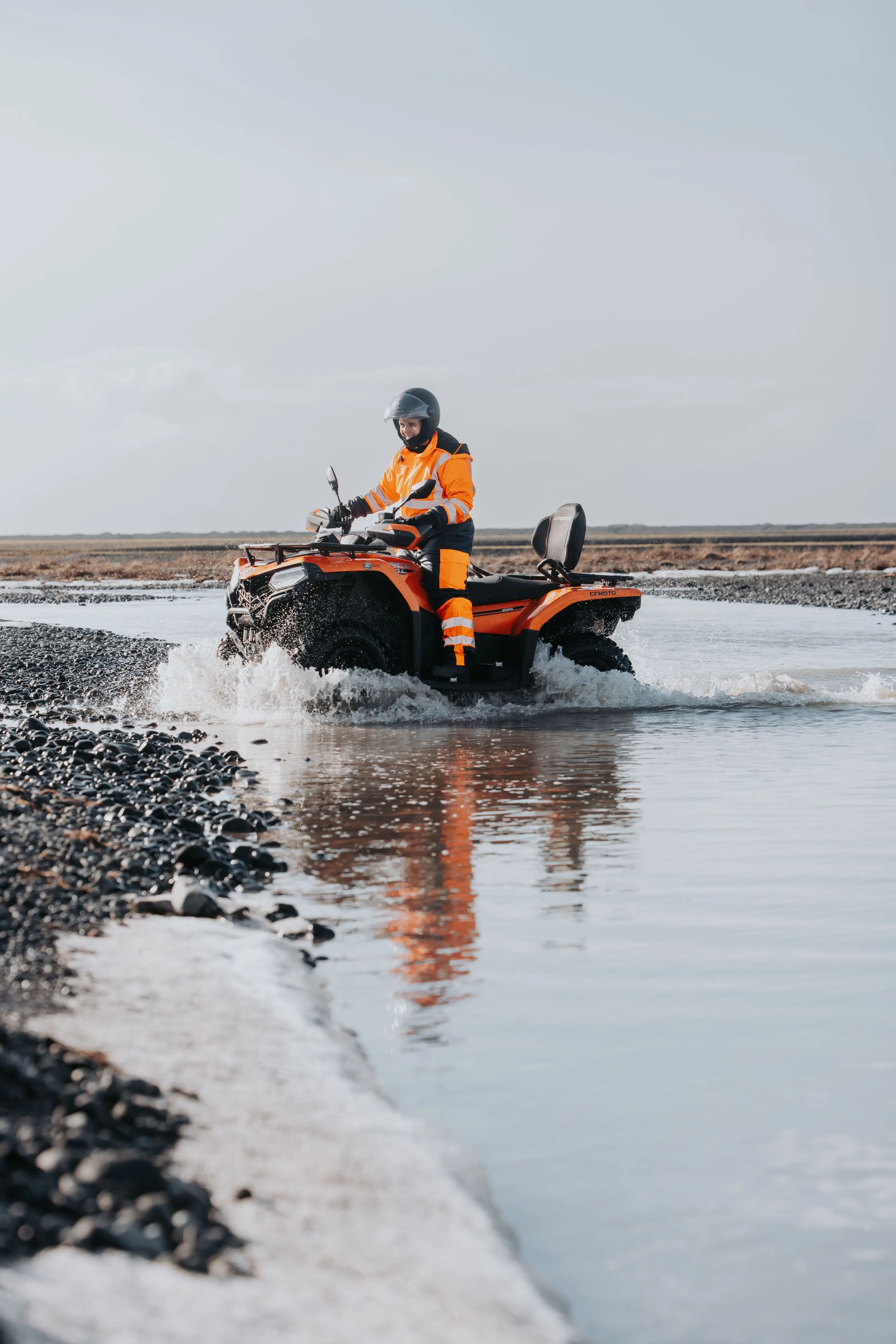 A single ATV rider slowly approaches the edge of the river bank after crossing with minimal splashing.