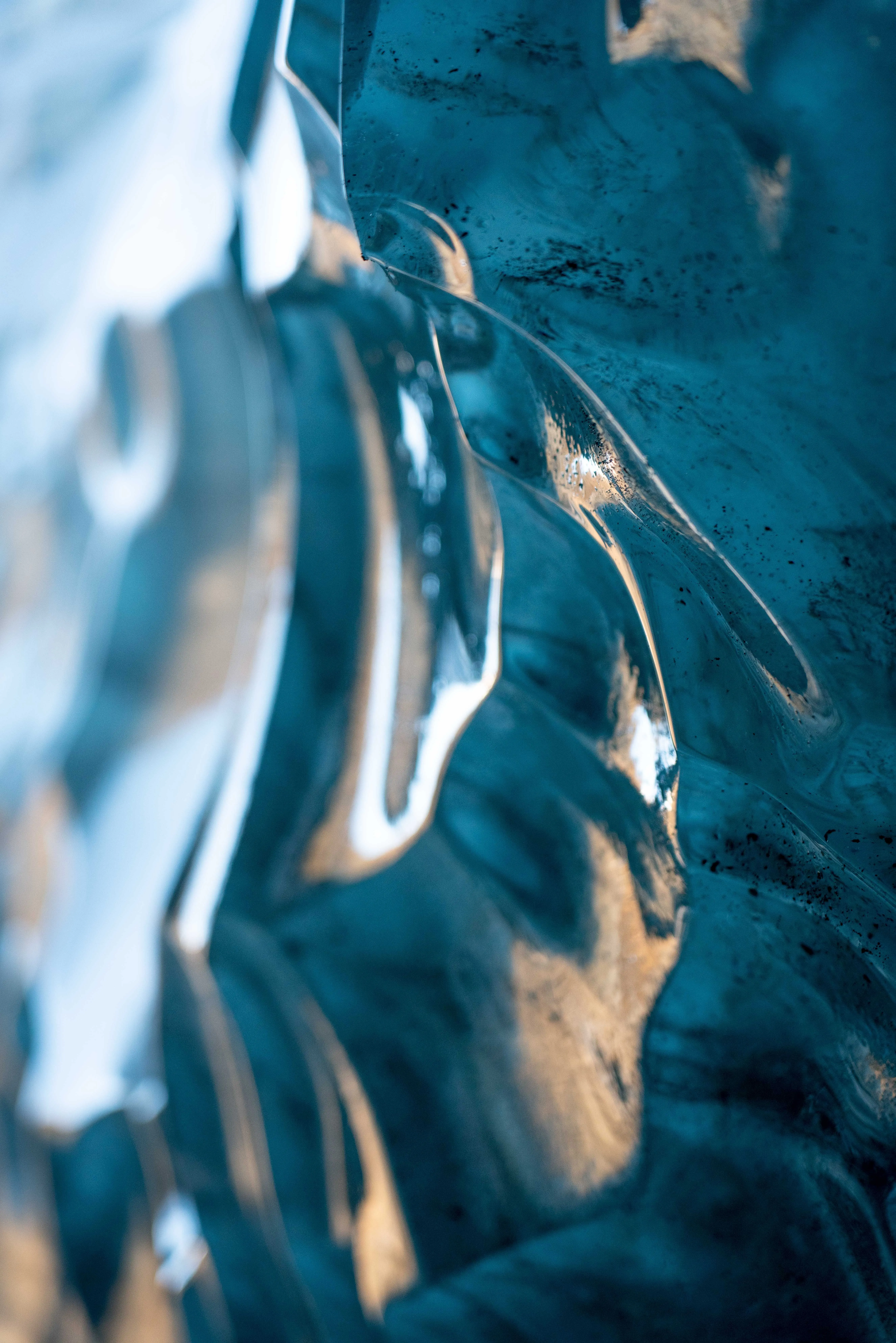 A vibrant blue glacial ice wall looks like ocean waves made of glass shimmering with warm, yellow sunlight.