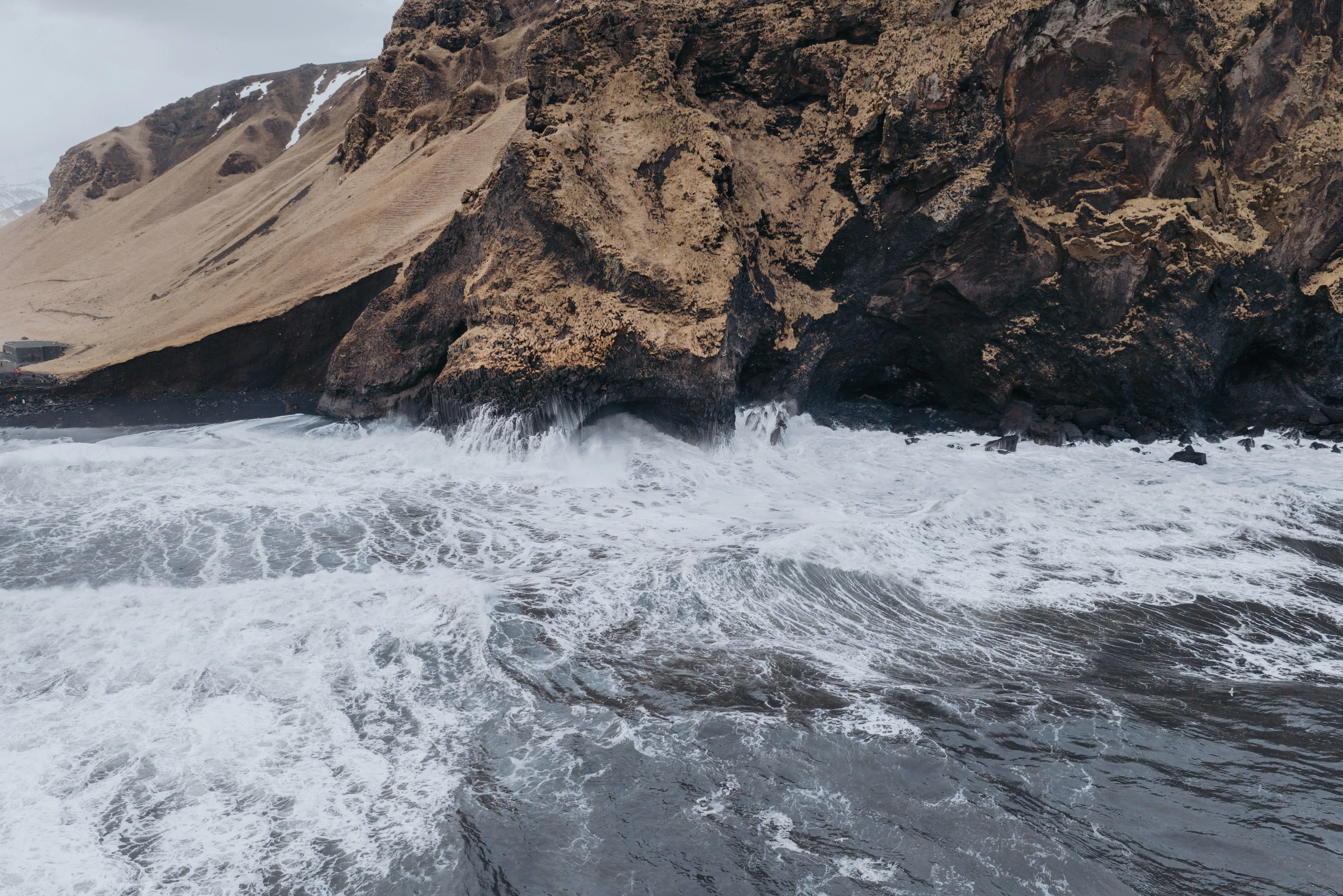 A view out over the ocean  of the tumultuous waves at the Black Sand Beach colliding with basalt column cliffs.
