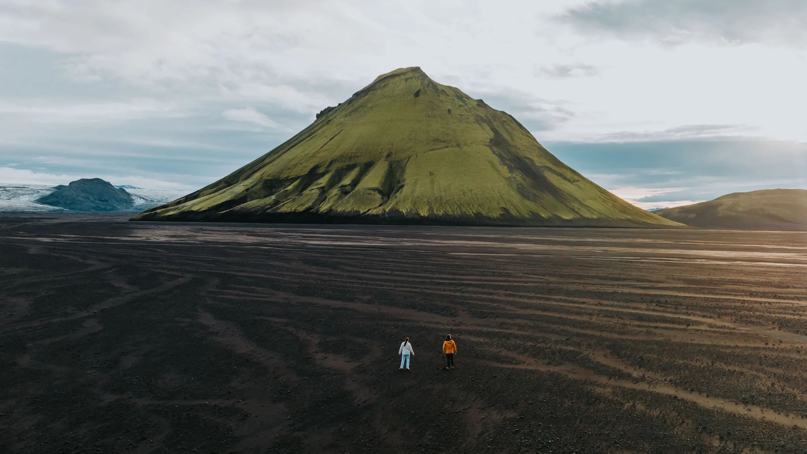 Two people stand in front of a vibrant green volcano in the otherwise vast landscape in the Icelandic highlands.