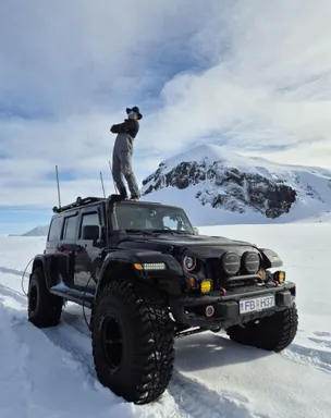 The guide stands on top of his black super jeep on a snowy road in the Icelandic Highlands.