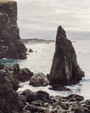 A sharp, triangular rock pinnacle juts out the ocean just beyond the cliff-lined coast.