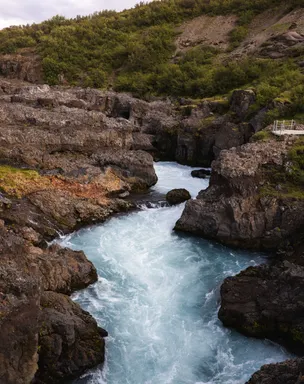A Light blue waterfall cascades through a narrow gorge, its appearance more akin to tumultuous river rapids.