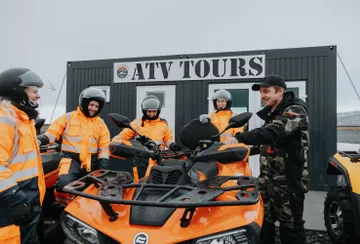 The guide briefs four riders wearing warm orange coveralls on the ATV controls before the ride.