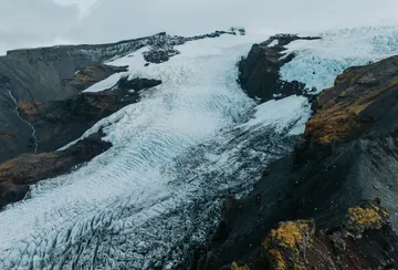 An aerial view of the ice fall and blue tinted crevasses in the steep upper section of Falljökull glacier look like huge waves flowing down the glacial valley.