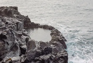 The ocean surrounds a small, natural pool cut out of rocky cliffs at the peninsula's edge.