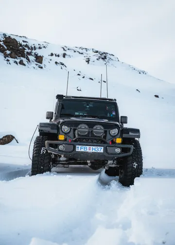 A black super jeep on a snowy road in the Icelandic highlands with a snow covered mountain in the background.