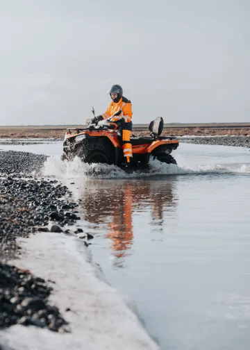 A single ATV rider slowly approaches the edge of the river bank after crossing with minimal splashing.