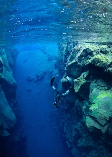 A freediver swimming down into a deep fissure with a sandy bottom.