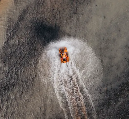 A person on an ATV rides through a glacial river creating a wake and making a large splash. 