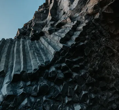 Deep black hexagonal basalt columns at the black sand beach tower over head, contrasting with the blue sky.