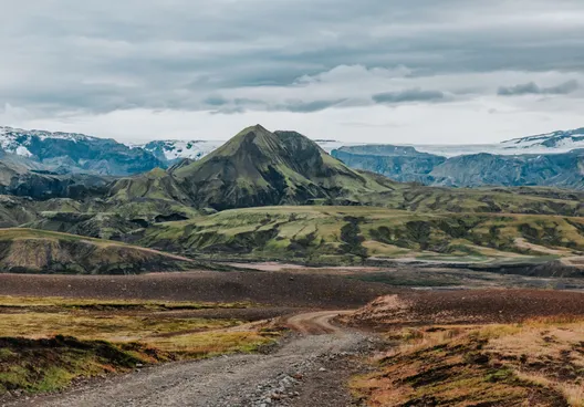 A lone F-road in the rugged Icelandic highlands, with a moss covered peak in front of Langjökull glacier in the distance.