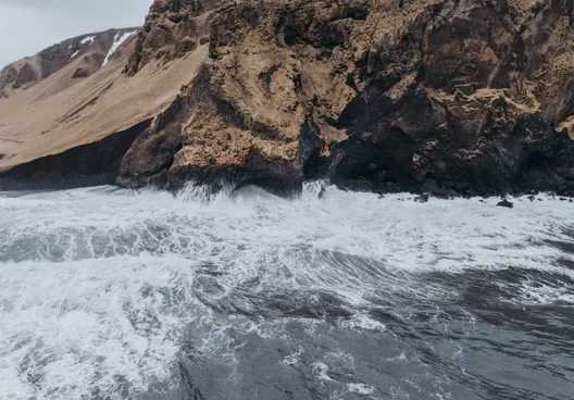 A view out over the ocean  of the tumultuous waves at the Black Sand Beach colliding with basalt column cliffs.