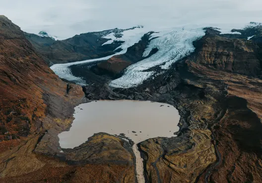 Two adjacent glaciers flow from the Vatnajökull ice cap toward a small glacial lagoon surrounded by yellow and orange moss-covered terrain on an autumn day.