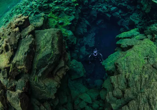 A solo free diver looks towards the surface from the depths of Silfra.