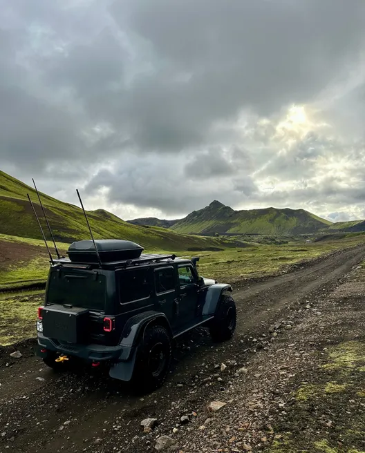 Black super jeep driving on a rocky Icelandic F-road through a vibrant green moss-covered mountainous landscape.
