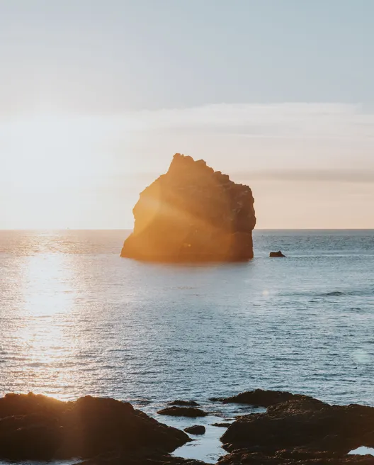 A small, jagged island just off the coast of Iceland's Reykjanes Peninsula as sunset is nearing, casting an orange glow on the water.