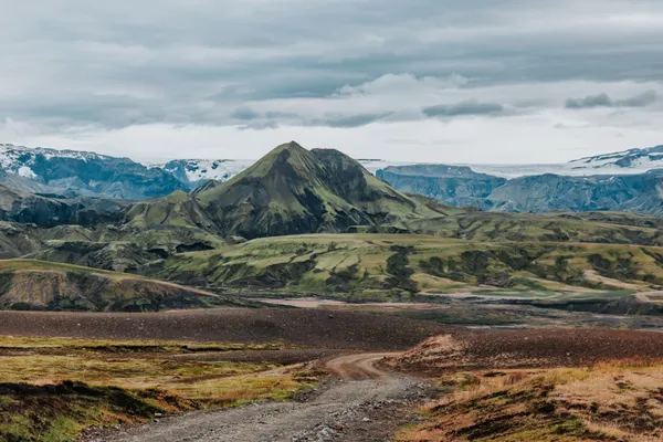 A lone F-road in the rugged Icelandic highlands, with a moss covered peak in front of Langjökull glacier in the distance.