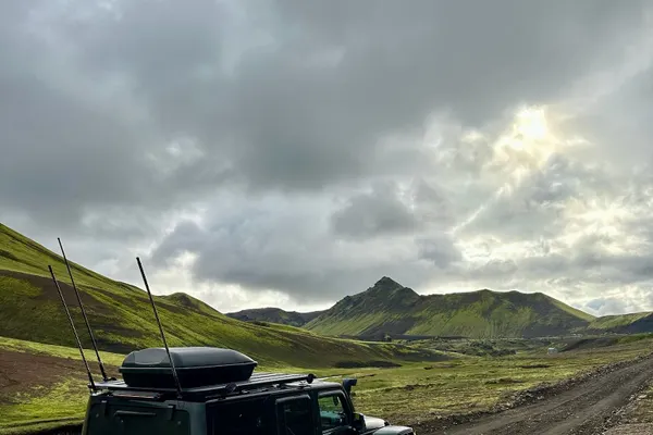 Black super jeep driving on a rocky Icelandic F-road through a vibrant green moss-covered mountainous landscape.