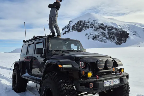 The guide stands on top of his black super jeep on a snowy road in the Icelandic Highlands.