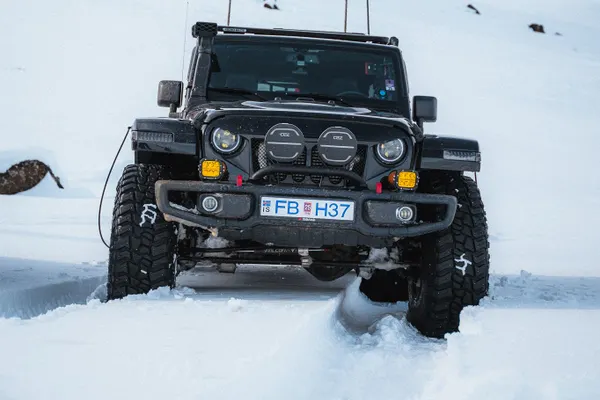 A black super jeep on a snowy road in the Icelandic highlands with a snow covered mountain in the background.