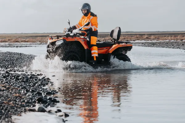 A single ATV rider slowly approaches the edge of the river bank after crossing with minimal splashing.