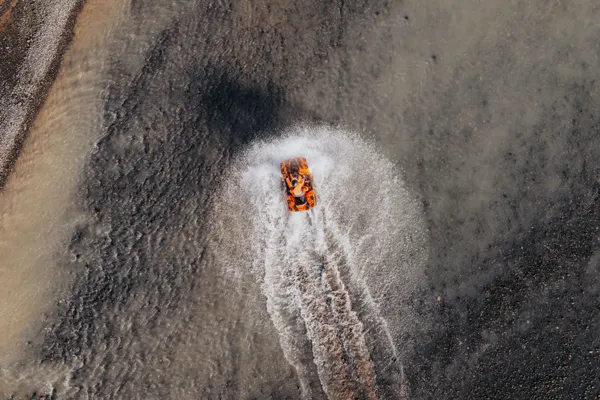 A person on an ATV rides through a glacial river creating a wake and making a large splash. 