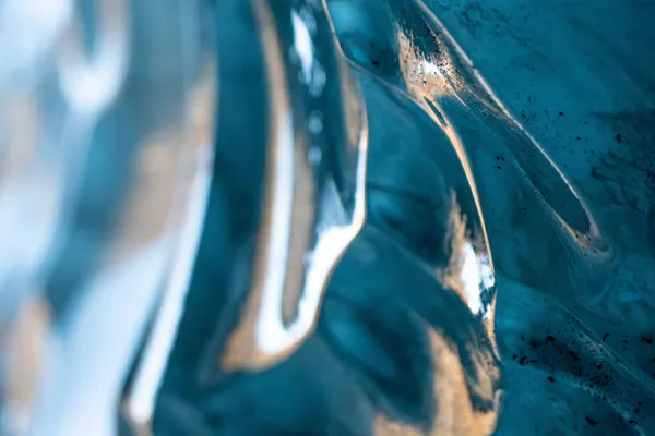 A vibrant blue glacial ice wall looks like ocean waves made of glass shimmering with warm, yellow sunlight.