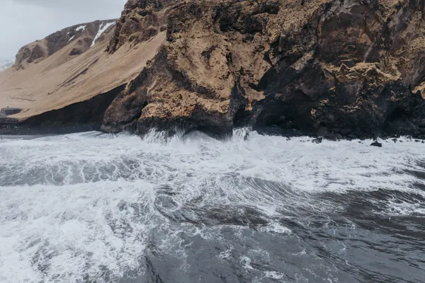 A view out over the ocean  of the tumultuous waves at the Black Sand Beach colliding with basalt column cliffs.