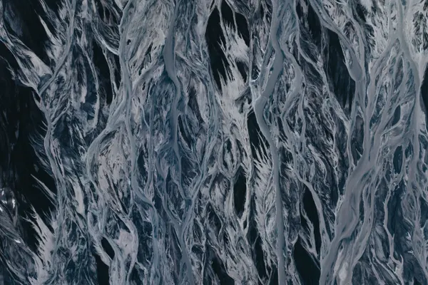 Hundreds of small, light blue glacial river streams flow over deep black volcanic sand in a unique weave-like pattern.