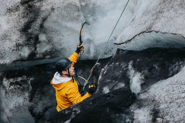 A client on an ice climbing tour starts climbing up a glacial wall that has a wide band of black, volcanic ash imbedded in the ice.