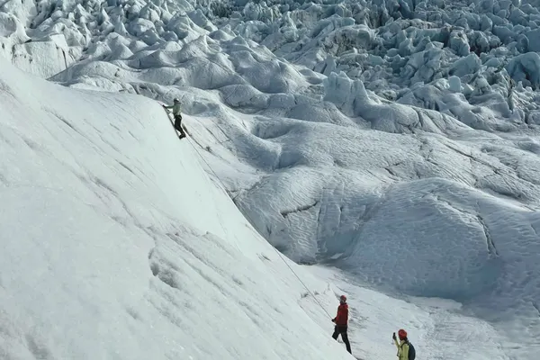 A client on an ice climbing tour reaches the top of a glacial wall on Falljökull.