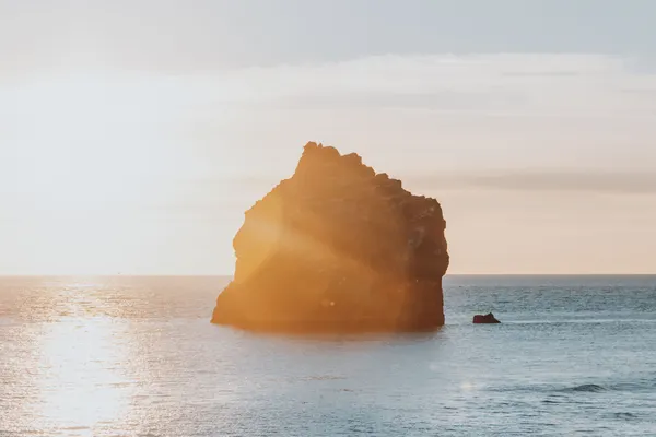 A small, jagged island just off the coast of Iceland's Reykjanes Peninsula as sunset is nearing, casting an orange glow on the water.
