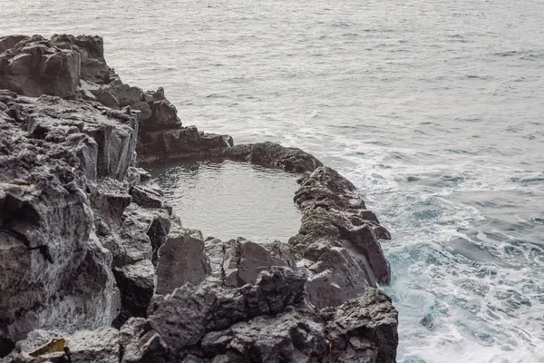 The ocean surrounds a small, natural pool cut out of rocky cliffs at the peninsula's edge.