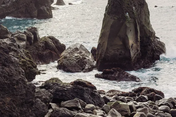 A sharp, triangular rock pinnacle juts out the ocean just beyond the cliff-lined coast.
