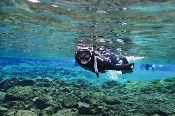 A snorkeler smiling under the clear water just below the surface, explores a shallow part of silfra.