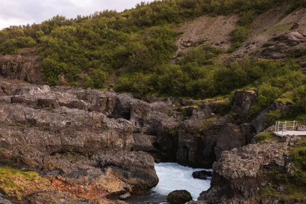 A Light blue waterfall cascades through a narrow gorge, its appearance more akin to tumultuous river rapids.