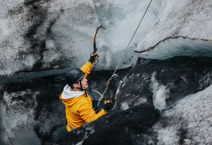 A client on an ice climbing tour starts climbing up a glacial wall that has a wide band of black, volcanic ash imbedded in the ice.