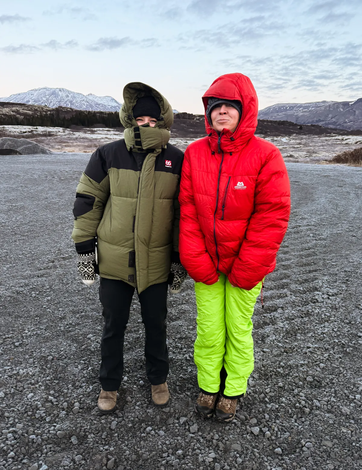 Two people wearing huge puffy jackets stand in a parking lot at Thingvellir in winter time.
