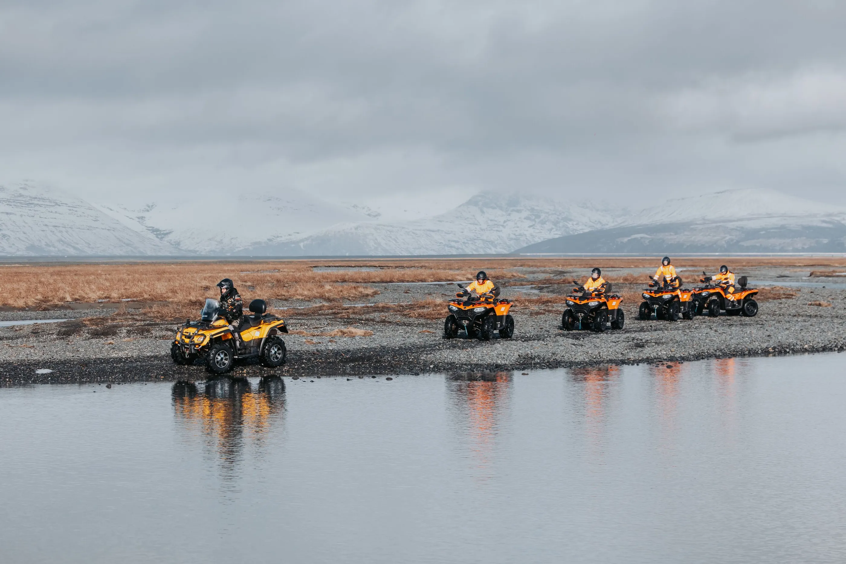 People on an ATV tour ride along side a river with Vatnajökull ice cap in the background.