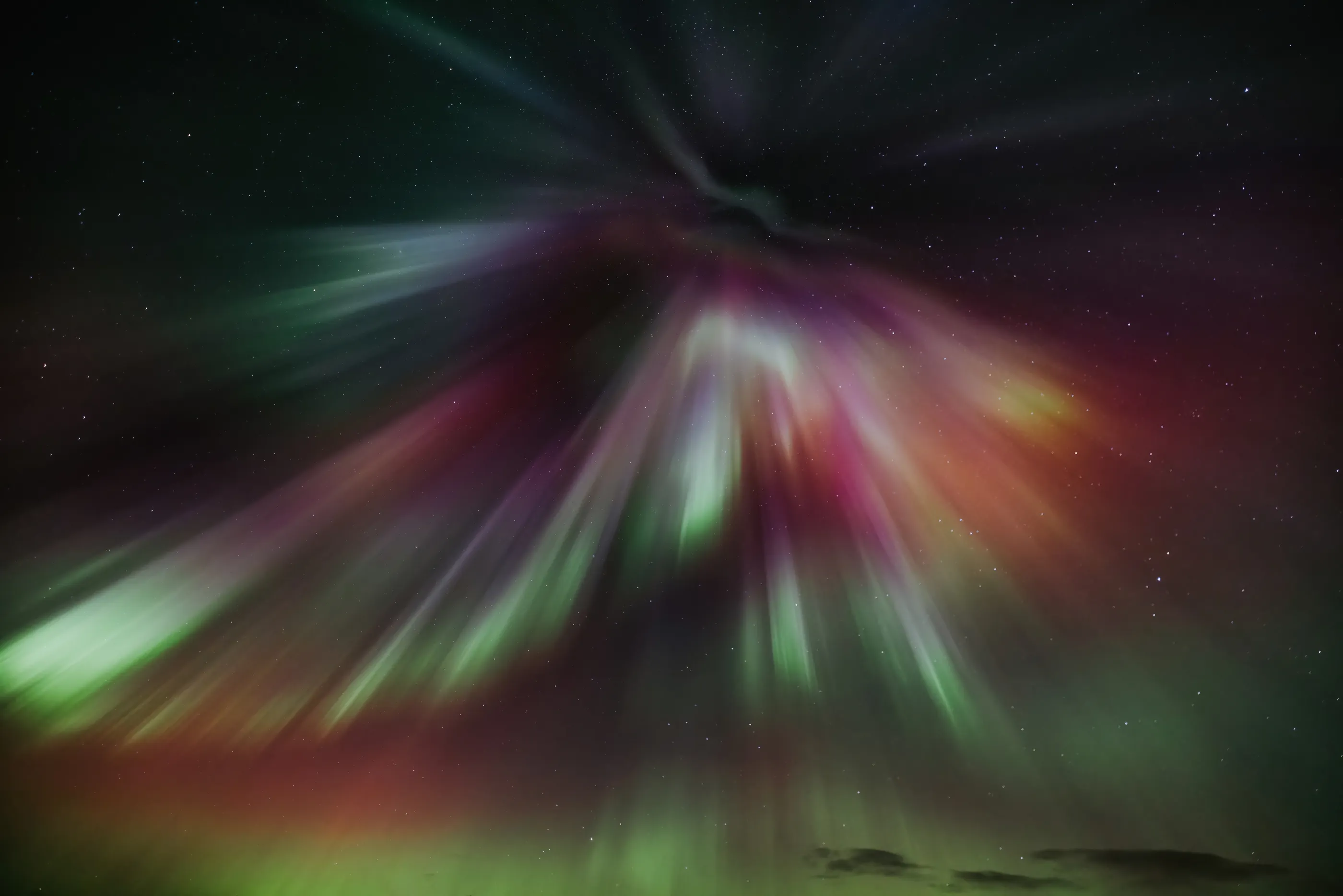 A very vibrant aurora of pink, green, orange and red bursts in the sky like a giant, colorful firework.