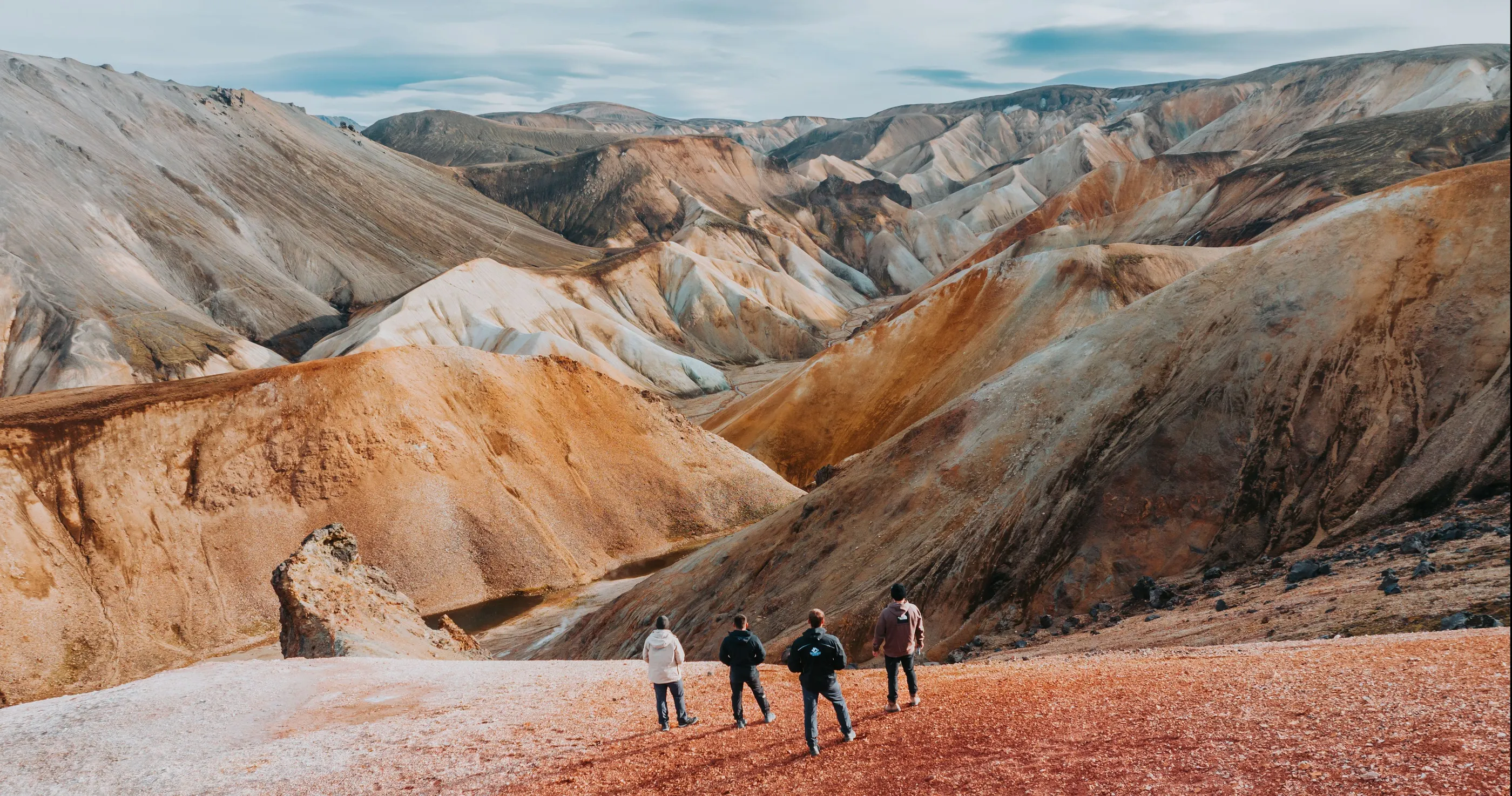 Four people admire the view of the colorful mountains of Landmannalaugar in the Icelandic Highlands.