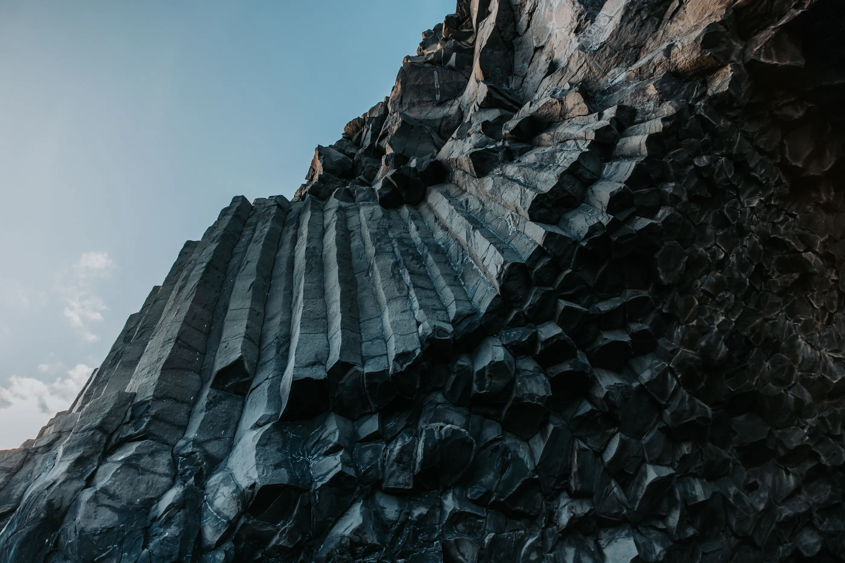 Deep black hexagonal basalt columns at the black sand beach tower over head, contrasting with the blue sky.
