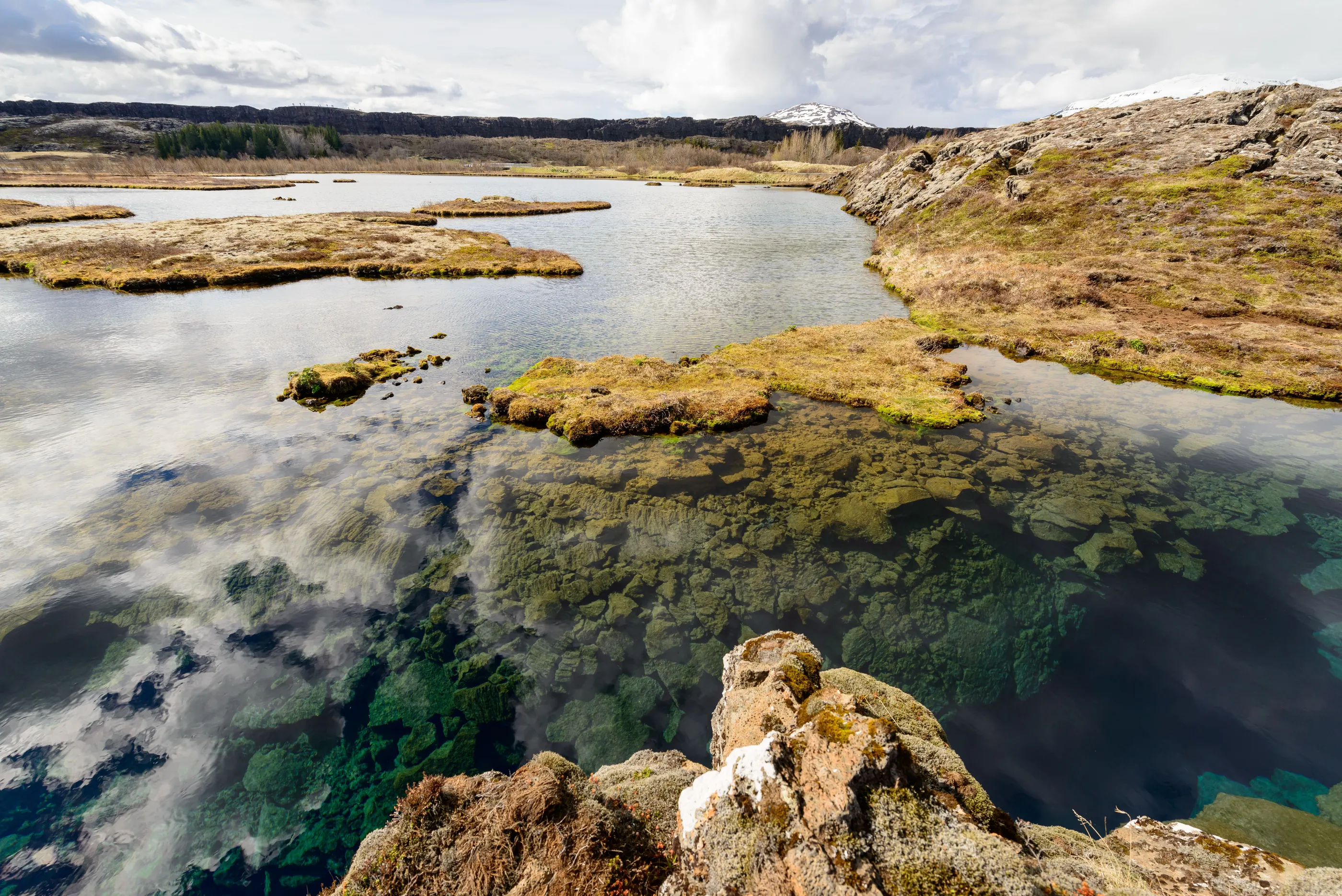 Clouds reflect on the deep, vibrant blue-green water of Silfra at the edge of Lake Thingvallavatn.