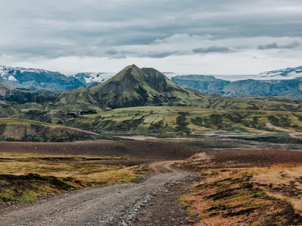 A lone F-road in the rugged Icelandic highlands, with a moss covered peak in front of Langjökull glacier in the distance.