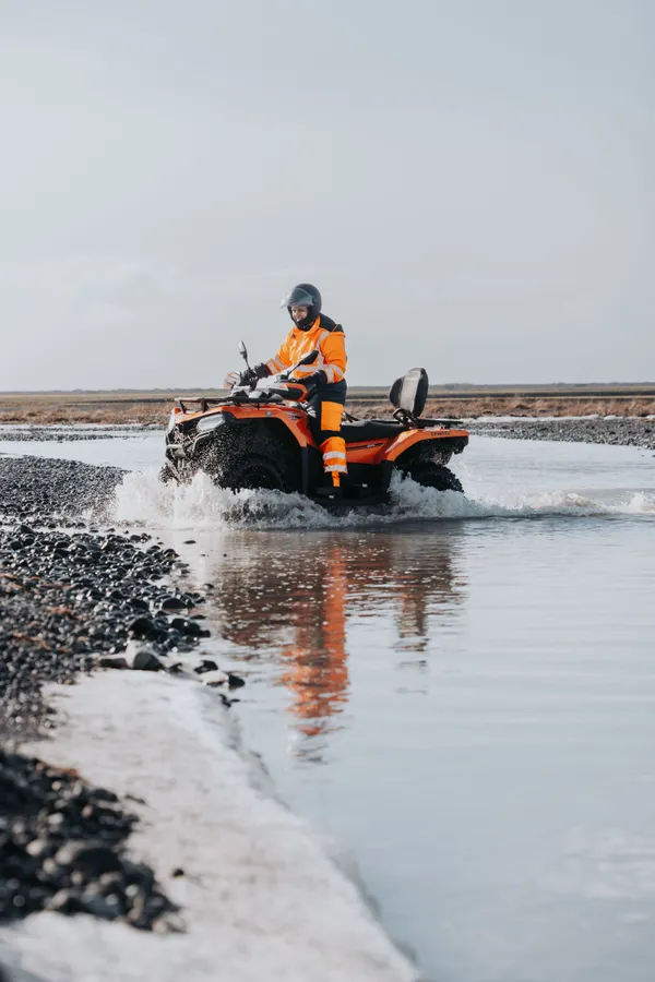 A single ATV rider slowly approaches the edge of the river bank after crossing with minimal splashing.
