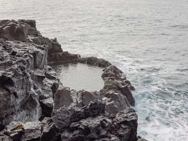 The ocean surrounds a small, natural pool cut out of rocky cliffs at the peninsula's edge.