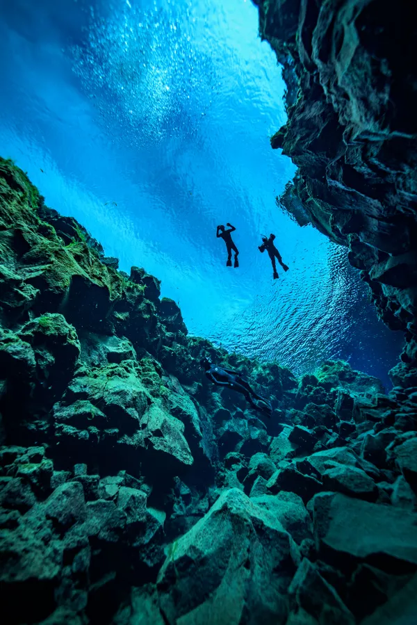 Sillouettes of two freedivers up on the surface of Silfra's vibrant blue waters between rocky fissure walls.