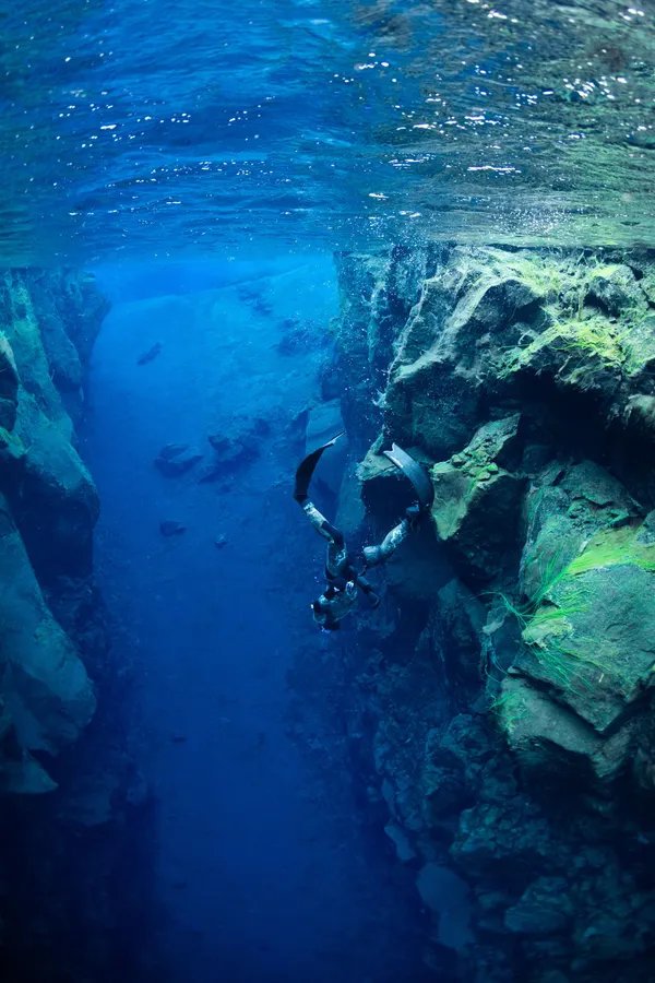 A freediver swimming down into a deep fissure with a sandy bottom.