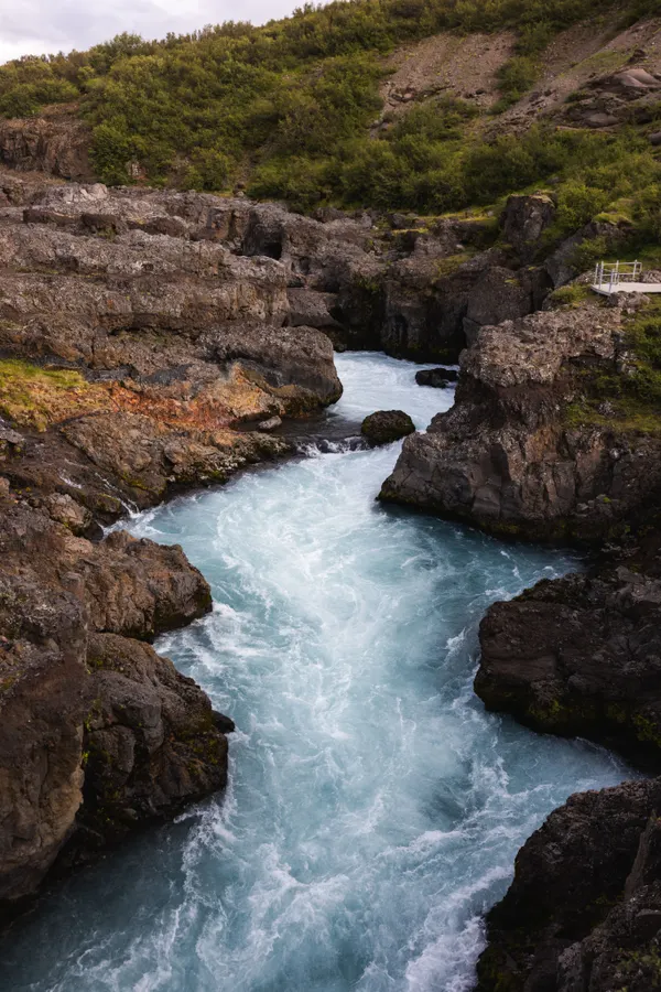 A Light blue waterfall cascades through a narrow gorge, its appearance more akin to tumultuous river rapids.